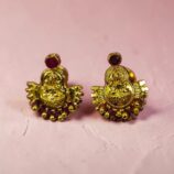 Celebrate tradition with these elegant Lakshmi Devi Stone Gold-Tone Stud Earrings, crafted to bring a divine and graceful charm to your jewelry collection. Featuring a beautifully detailed Lakshmi Devi motif at the center, these earrings symbolize prosperity, blessings, and timeless beauty. The rich gold-tone finish adds a luxurious shine, while the vibrant stone accent on top enhances their regal appeal. Designed with intricate craftsmanship, these traditional stud earrings are perfect for festive occasions, weddings, poojas, and cultural celebrations. Their lightweight and comfortable fit makes them ideal for long wear without compromising style. Pair them with sarees, lehengas, salwar suits, or ethnic gowns to complete your traditional look effortlessly. A perfect blend of devotion and fashion, these earrings also make a thoughtful gift for loved ones on special occasions like festivals, birthdays, and anniversaries. Add a touch of divine elegance to every outfit with these stunning Lakshmi Devi earrings.